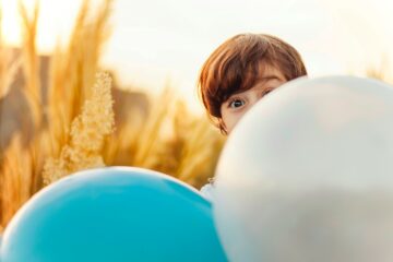 Junge schaut hinter bunten Luftballons hervor