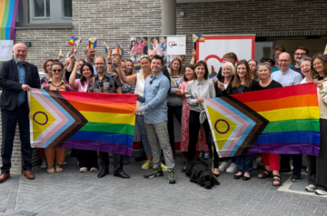 Gruppenfoto vor dem AWO-Haus: Die Teilnehmenden stehen gemeinsam vor zwei großen Regenbogenfahnen. Jede Person hält eine kleine Pride-Flagge in der Hand.
