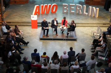 Fishbowl-Diskussion beim Jahresempfang der AWO Berlin in der Heilig-Kreuz-Kirche: Oliver Bürgel moderiert, neben ihm Raed Saleh und Expert*innen aus Politik und Praxis. Im Halbkreis um die Gesprächsrunde sitzt das Publikum.