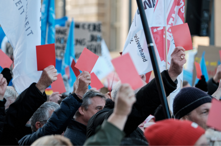 Das Foto zeigt Menschen bei einer Demonstration, die rote Karten hochhalten.