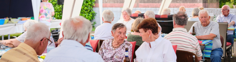 Das Foto zeigt eine Gruppe älterer Menschen, die bei einer Veranstaltung zusammensitzen und sich unterhalten.